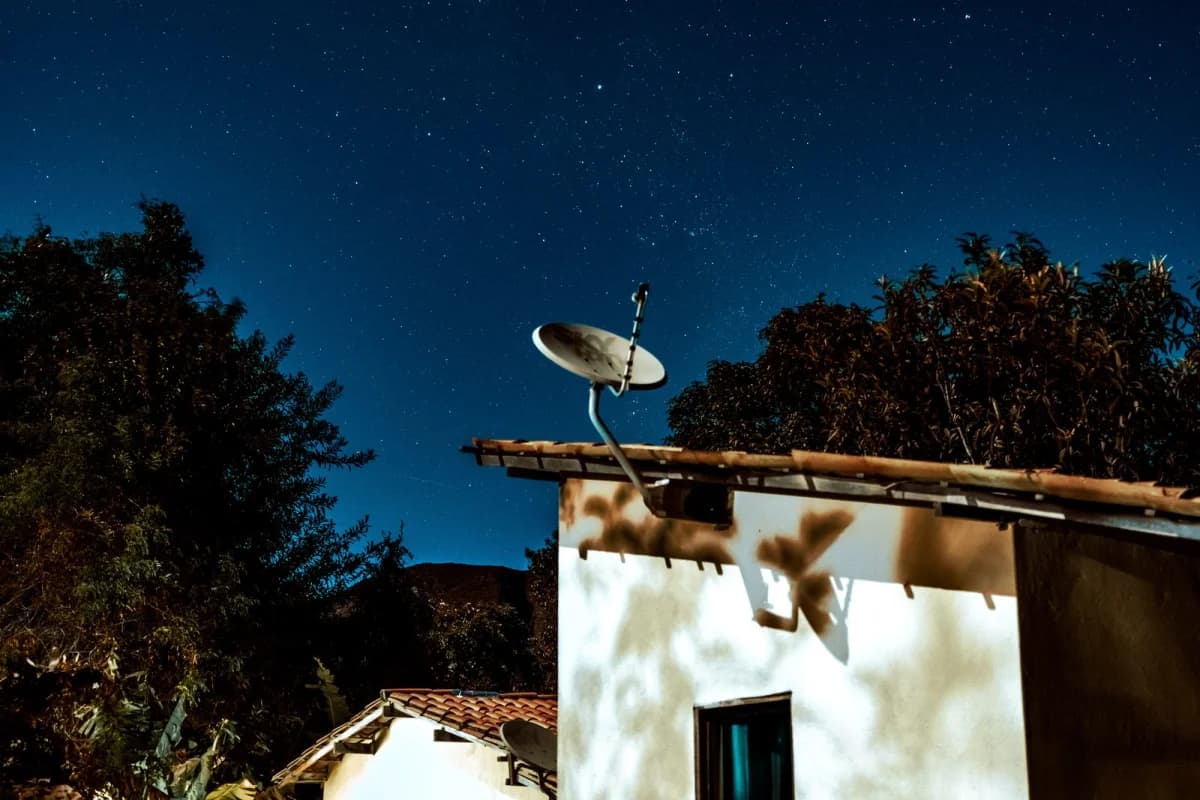A satellite dish on a rural house roof under a starry night sky