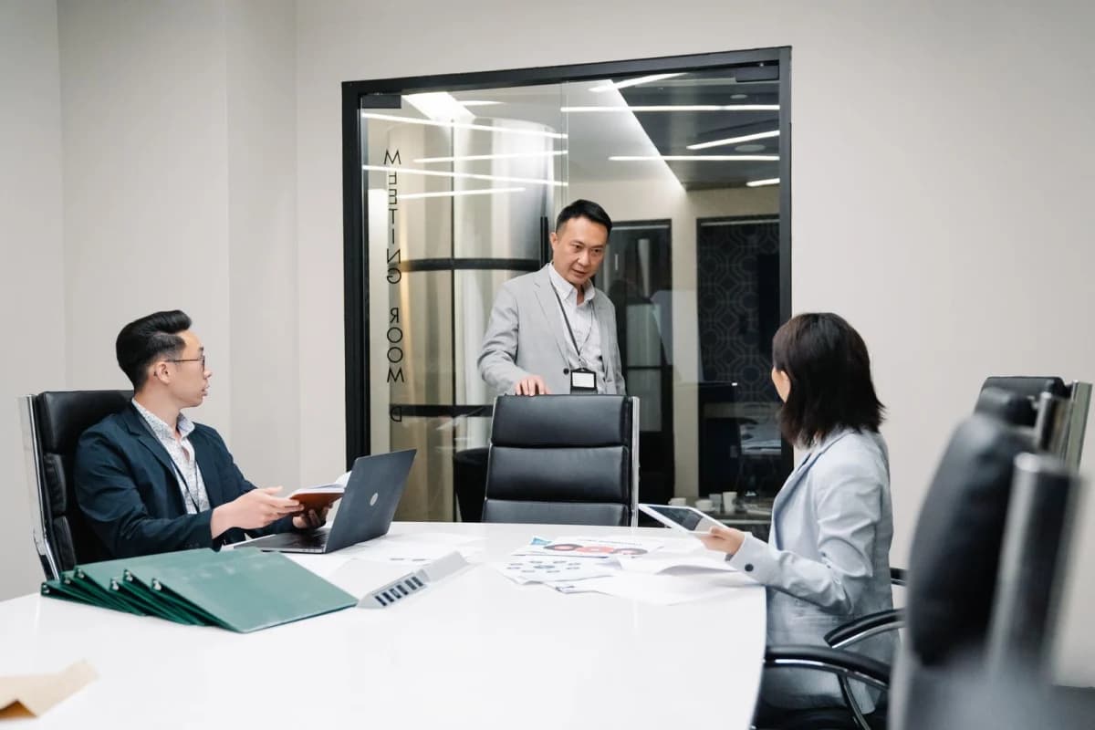 Employees working at desks in a modern office with laptops and morning light through large windows