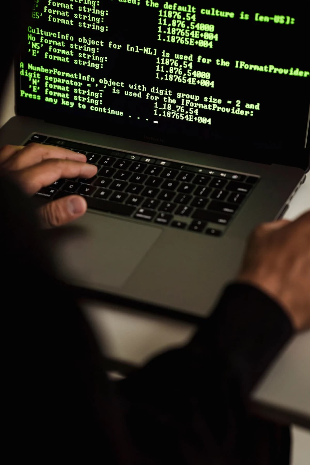 Close-up of a hacker's hands typing on a laptop in a dark room, representing AI-powered phishing attacks