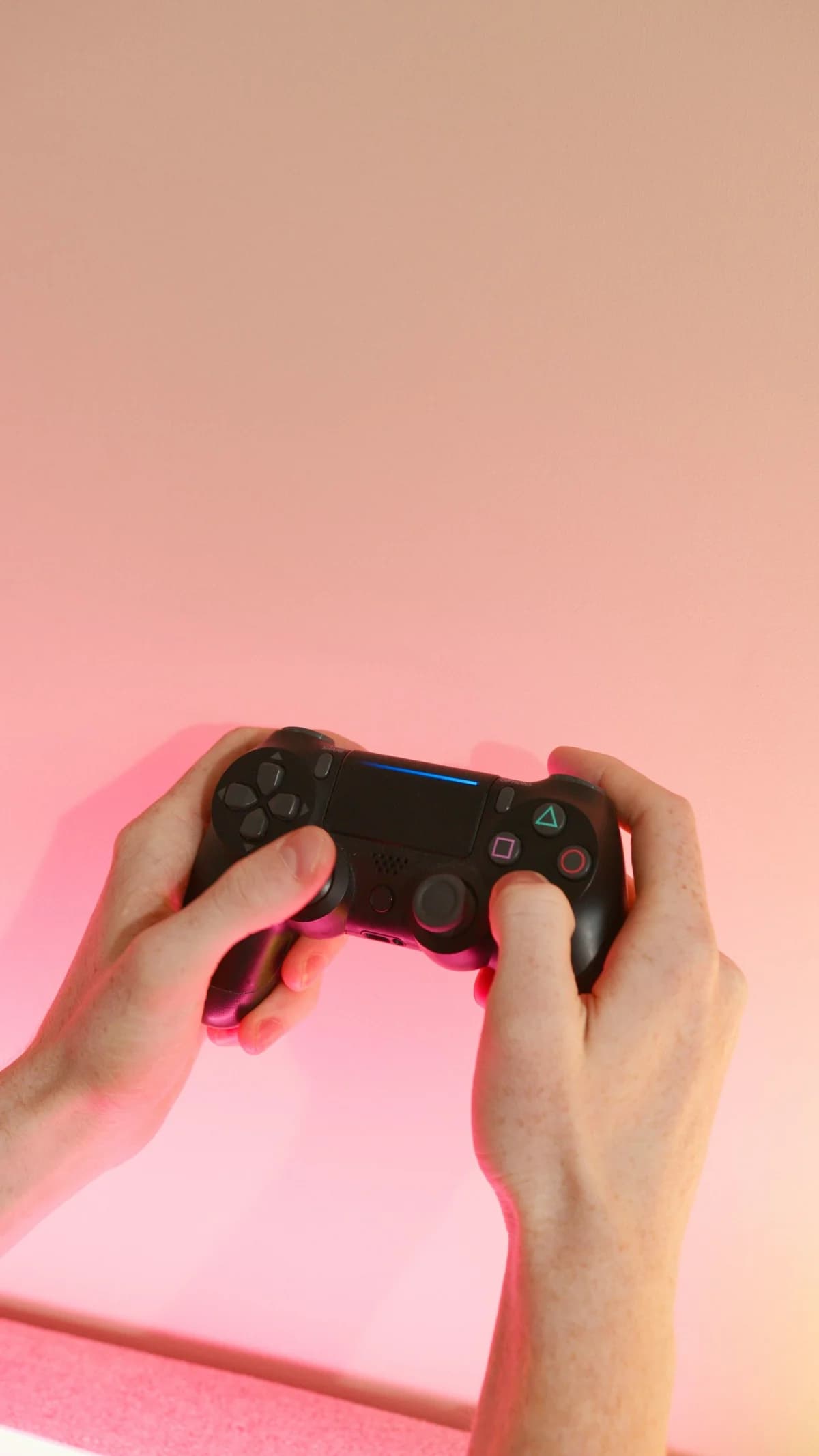 A person holding a wireless game controller against a pink background