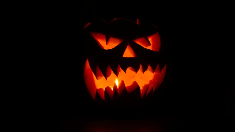 Dark home theatre with glowing TV, jack-o'-lantern and popcorn bowl in moody orange light