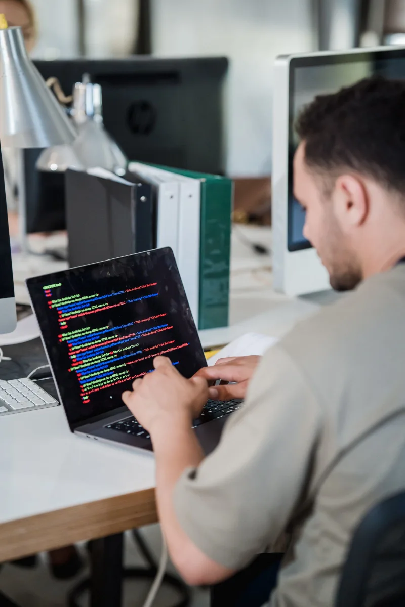 Professional at a desk with code on screen and city skyline through window