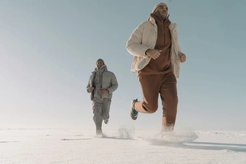A runner in winter gear jogging on a snow-covered path with visible breath in the cold air