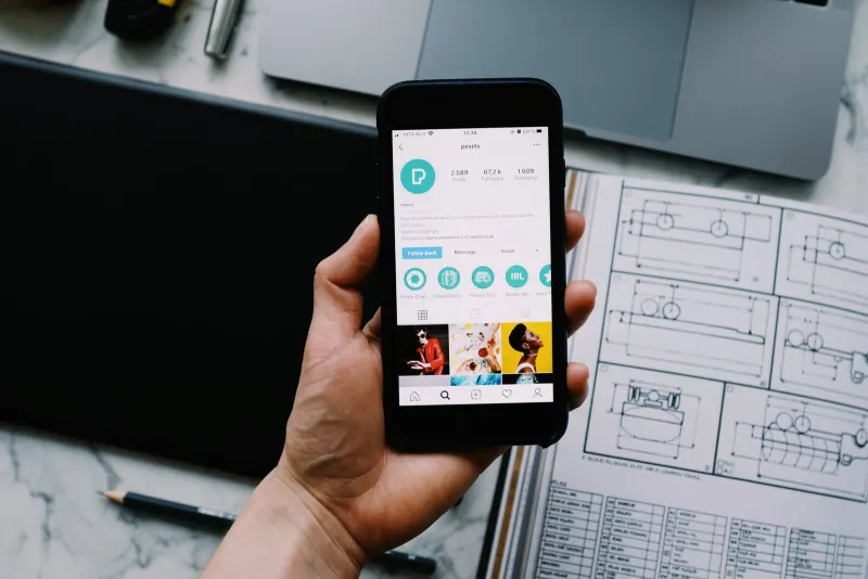 A hand holding a smartphone displaying apps, with tech gadgets on a desk, representing on-device AI in 2026